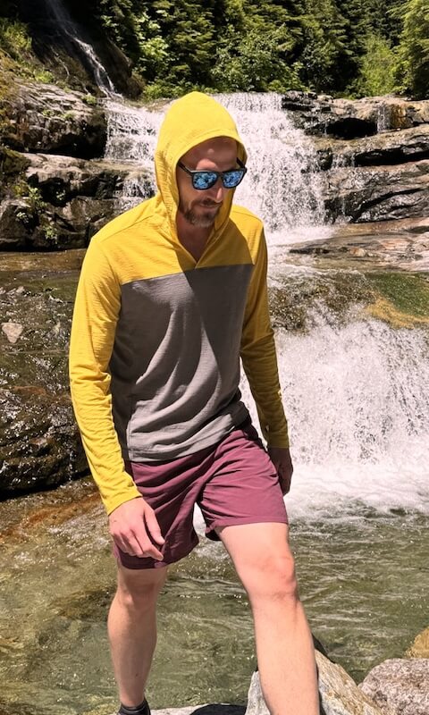 Hiker wearing a two-tone sun hoodie standing in front of a waterfall