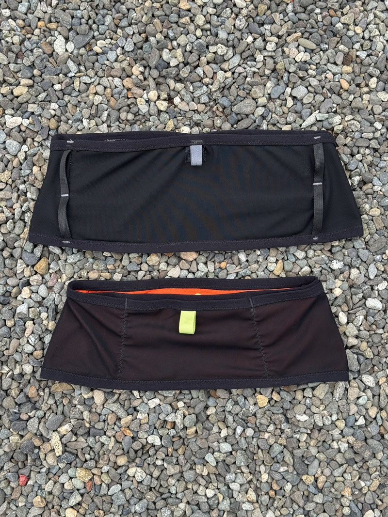 Two variants of a DIY running vest laid out on a pebble beach.